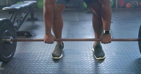 African man gripping barbell and preparing deadlift on gym floor, wearing smartwatch