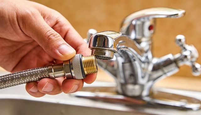 Hand connecting braided hose to chrome faucet aerator with brass coupling closeup