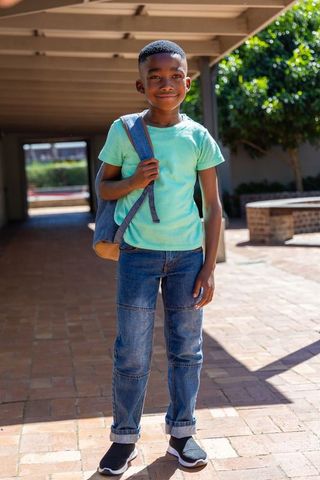 Smiling african american boy carrying backpack on sunlit school courtyard pathway