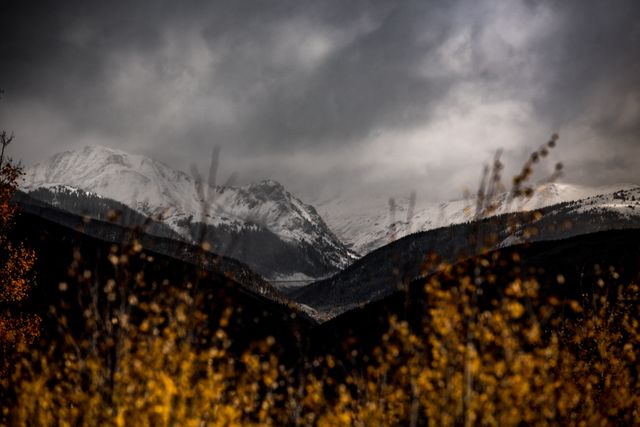 Depicting rugged beauty of snow-capped mountains, this photo conveys a moody and dramatic atmosphere with stormy clouds hovering over the peaks. Ideal for use in nature magazines, adventure blogs, or any publication focusing on outdoor activities. It captures the essence of wilderness and natural resilience, making it suitable for themes centered around remote getaways, hiking, or environmental awareness.