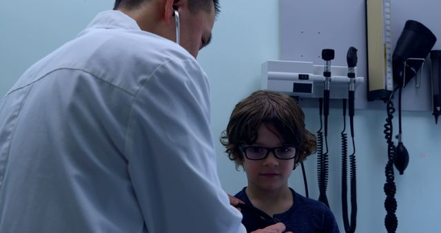 Young boy patiently receives medical examination from a pediatrician using a stethoscope in clinical exam room. Ideal for illustrating healthcare, pediatric care, child health, doctor visits, and medical consultations. Suitable for use in health-related articles, promotional material for pediatric services, and educational resources about child health maintenance and doctor-patient interactions.