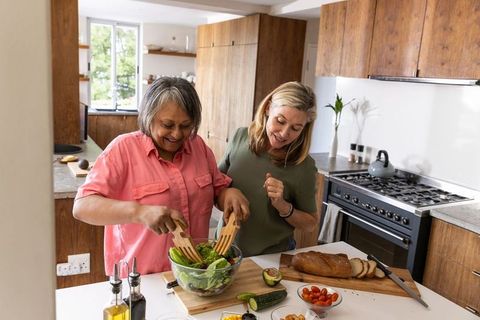 Diverse female friends preparing salad together in modern kitchen