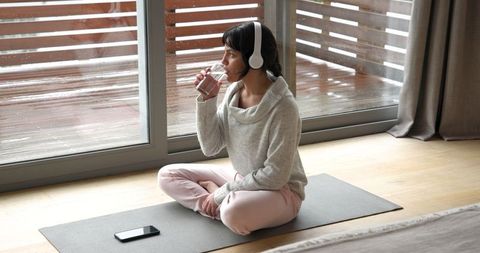 Woman Relaxing on Yoga Mat Drinking Water With Headphones