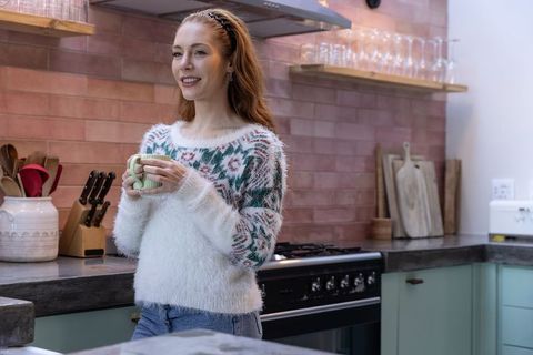 Woman smiling in modern kitchen holding drink in ceramic mug