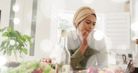 Woman wearing headscarf watching smartphone in bright kitchen