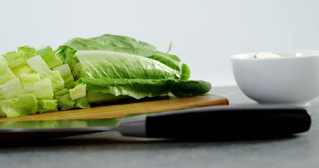 Freshly chopped romaine lettuce on wooden cutting board next to knife. Ideal for content about healthy eating, cooking tutorials, meal preparation, vegetarian recipes, or organic food articles. Perfect for shops selling kitchen utensils or fresh produce.