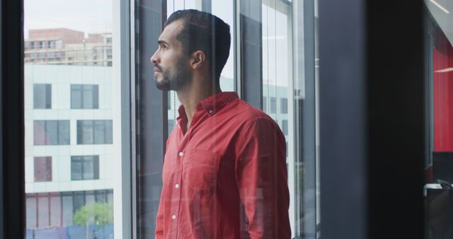 Contemplative Man in Red Shirt Gazing Out of Office Window - Download Free Stock Images Pikwizard.com