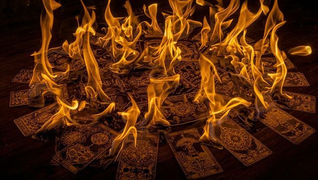Tarot card circle burning with dramatic orange flames and charred edges on dark wood
