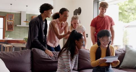 Friends celebrating surprise card moment on living room sofa, joyful reactions