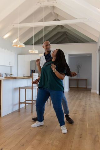 African american couple dancing joyfully in modern vaulted kitchen with natural light