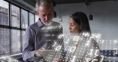 Two professionals reviewing tablet with digital binary overlay in modern office loft