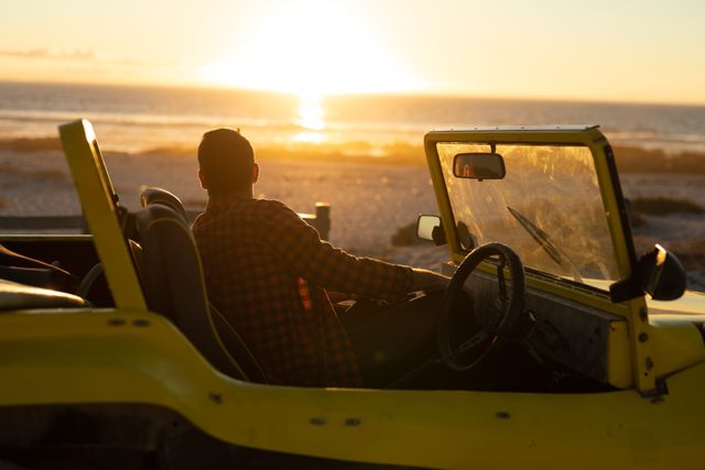 Caucasian man sitting in beach buggy on beach at sunset admiring the view. beach stop off on summer holiday road trip.
