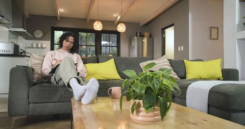 Non-binary person writing in notebook on sofa in cozy modern open-plan living room