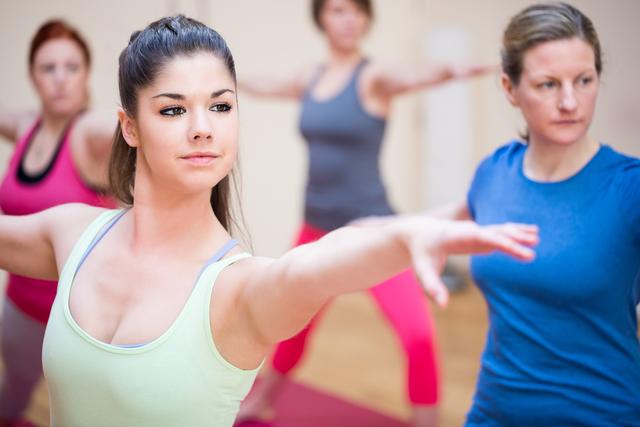 Women practicing yoga in a fitness studio, focusing on balance and flexibility. Ideal for use in articles or advertisements related to fitness, wellness, healthy lifestyle, and group exercise classes.