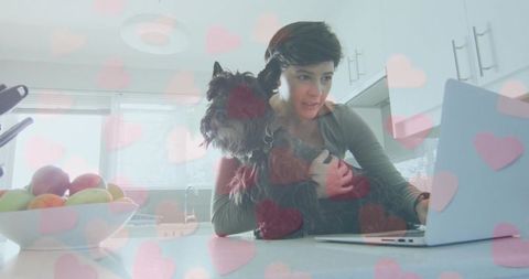 Woman Holding Terrier While Typing on Laptop at Kitchen Counter with Pink Heart Overlay