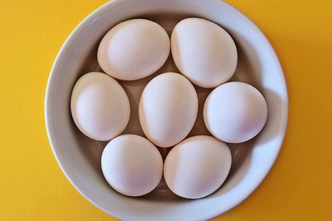 Top-down arrangement of seven white eggs nesting in ceramic bowl on bright yellow surface