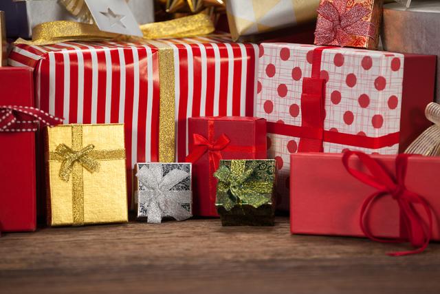 Various colorful wrapped gift boxes with ribbons and bows are arranged on a wooden table, creating a festive atmosphere. Ideal for holiday season promotions, Christmas advertisements, festive greeting cards, and holiday-themed blog posts.