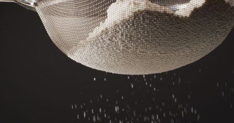 Sifting Flour through Sieve on Black Background