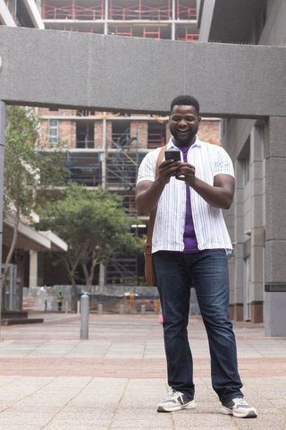 African american man standing in city plaza checking smartphone near construction site