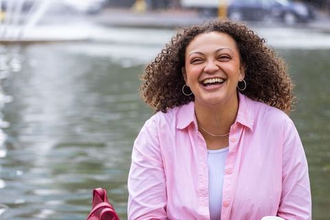 Laughing african american woman enjoying waterfront moment in pink shirt and hoop earrings