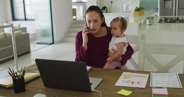 Caucasian mother holding her baby and talking on smartphone while working from home. motherhood, love and childcare concept