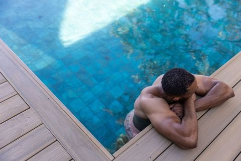 Muscular african american man resting on wooden deck by blue mosaic pool