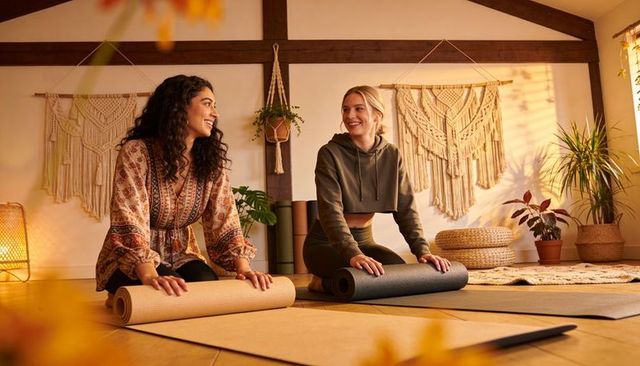 Unrolling yoga mats at home two women chatting in boho macrame studio with plants