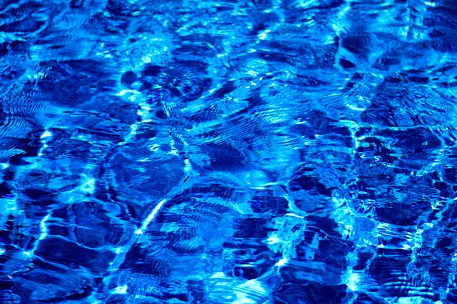 Close-up view of rippling blue pool water with mesmerizing sunlight reflections. Ideal for backgrounds, relaxation themes, aquatic visuals, and designs related to summer or leisure activities.