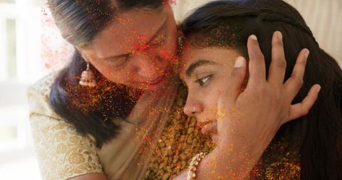 Indian mother embracing daughter, leaning foreheads together, celebrating with color powder