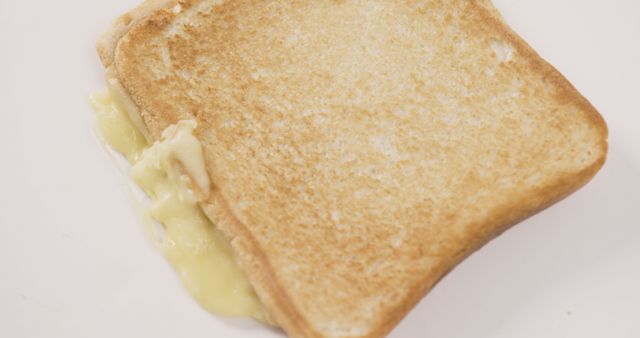 Close-up view of a grilled cheese sandwich with gooey melted cheese oozing between two pieces of golden brown toasted bread. Ideal for food blogs, recipe websites, and advertisements for breakfast or lunch meals. Could also be used in educational materials or content about quick and easy meal options.