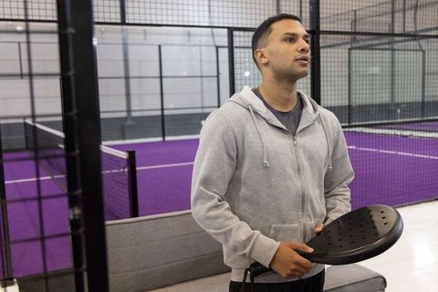 Young man holding padel paddle on indoor purple court preparing for match