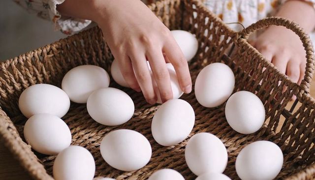 Child arranging white eggs in woven basket on wooden table rustic farmhouse breakfast