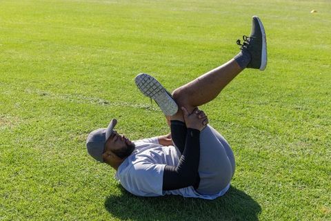 African american athlete stretching hamstring on grass field preworkout warmup routine