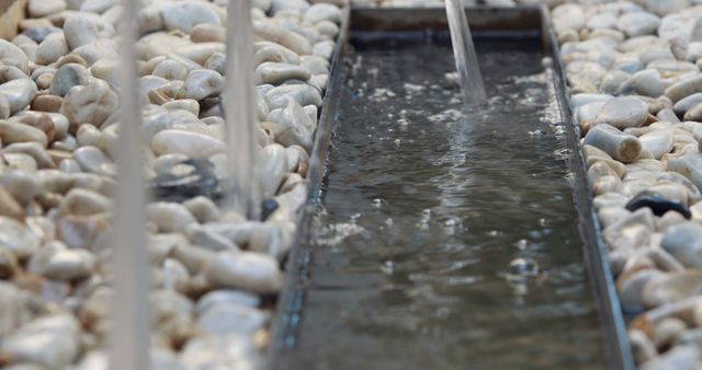 Close-up view of a water stream flowing through a section surrounded by smooth, white marble stones. This tranquil and soothing scene can be ideal for use in blogs, websites, or publications dealing with outdoor gardening, landscaping, zen gardens, spa environments, or relaxation techniques.