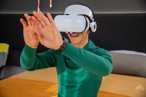 Young man wearing white vr headset reaching forward in modern coworking lounge workspace