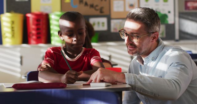 Diverse happy male teacher helping schoolboy sitting in classroom during learning. children in primary school.