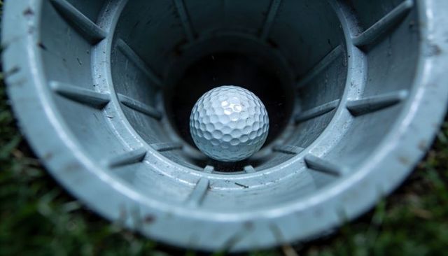 Golf ball nestled in cup liner closeup on putting green showing damp texture and grass