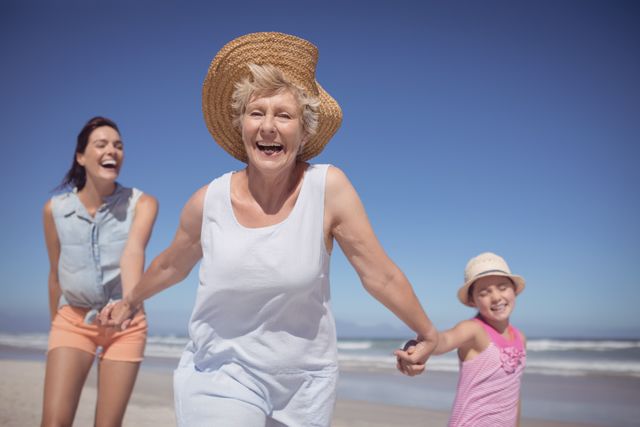 Three generations of women enjoying a sunny day at the beach. Grandmother, mother, and daughter are holding hands and smiling, creating a joyful and carefree atmosphere. Ideal for use in advertisements, travel brochures, family-oriented content, and lifestyle blogs to depict family bonding and summer fun.