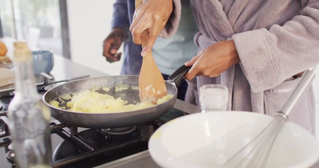 Couple cooking scrambled eggs on stovetop in modern kitchen. An intimate domestic moment emphasizing bonding and collaboration during breakfast preparation. Ideal for use in articles about home cooking, healthy eating, and fostering relationships through shared activities in the kitchen.