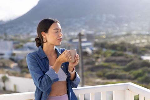 Young woman savoring morning coffee on balcony overlooking coastal town and mountain view