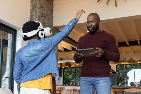 African american father guiding child using vr headset at home
