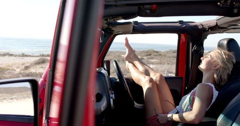 Young Woman Relaxing in Car on Scenic Beach Road Trip