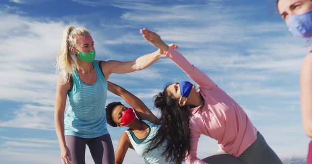 Women practicing yoga outdoors, observing social distancing and wearing face masks, symbolizing fitness during pandemic and healthy lifestyle. Perfect for articles on outdoor exercises, health benefits of yoga, pandemic safety measures, and group fitness activities.