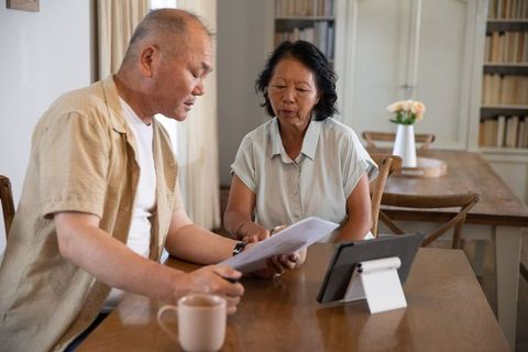 Asian senior couple reviewing financial documents at home using tablet and coffee