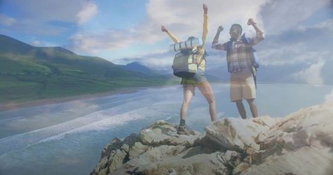 Celebrating hikers raising arms on rugged coastal cliff overlooking expansive sandy bay