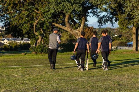 Coach leading young cricket players across grassy field carrying bats helmets and pads