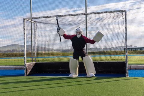 Field hockey goalkeeper in full protective gear on turf