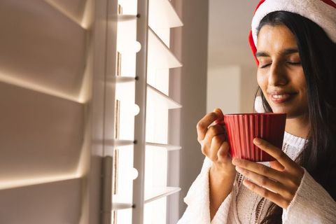 Woman Wearing Santa Hat Relaxing with Hot Beverage by Window