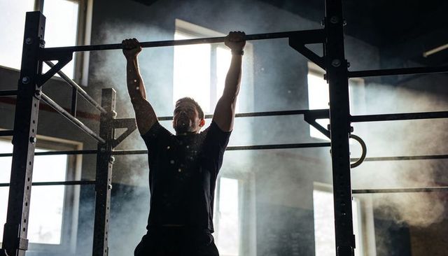 Backlit Adult Male Performing Pull-up on Industrial Rig with Chalk Dust, Grit and Intensity