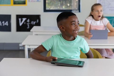 Smiling schoolboy using tablet while classmate holding tablet, engaging in digital learning